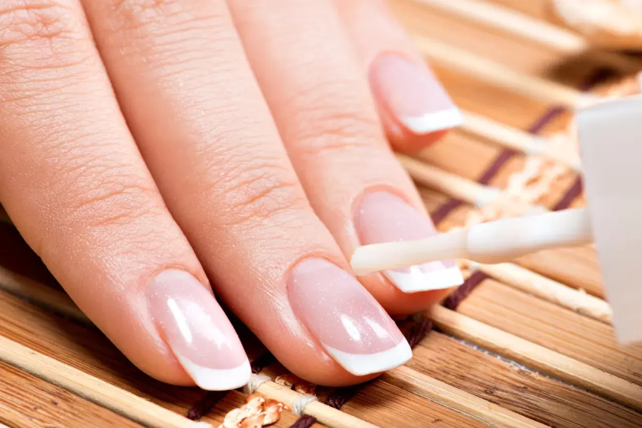 Dłoń z idealnym francuskim manicure, na paznokcie nakładana jest najlepsza odżywka do paznokci.