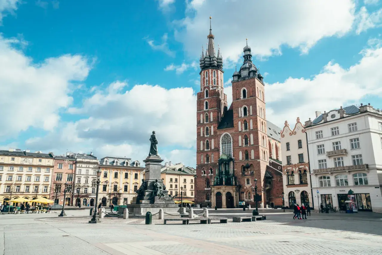 Rynek Główny w Krakowie z Kościołem Mariackim i pomnikiem Mickiewicza. Stare miasto Kraków tętni życiem pod błękitnym niebem.