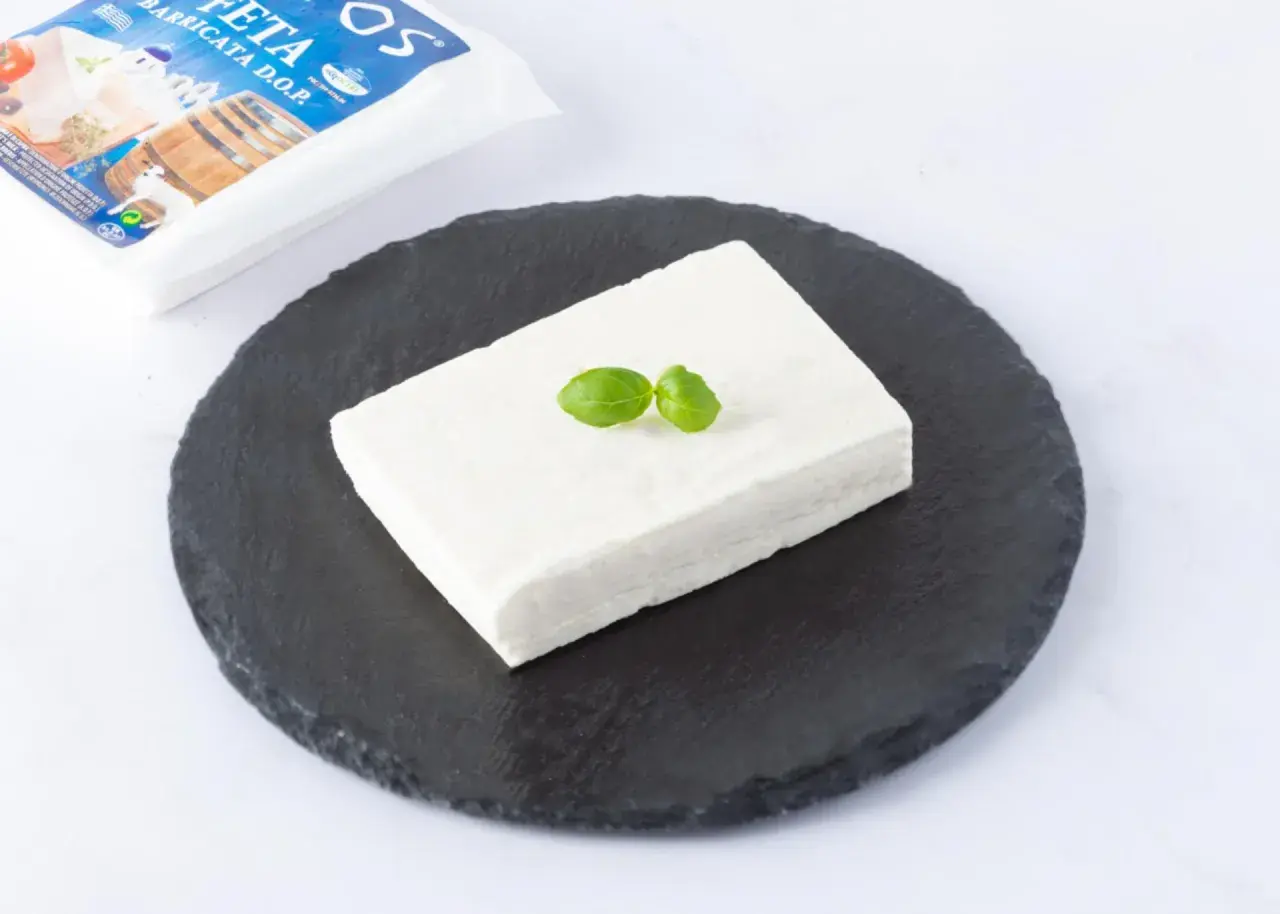 Un blocco di feta DOP su una pietra scura, guarnito con basilico. La confezione è visibile sullo sfondo.