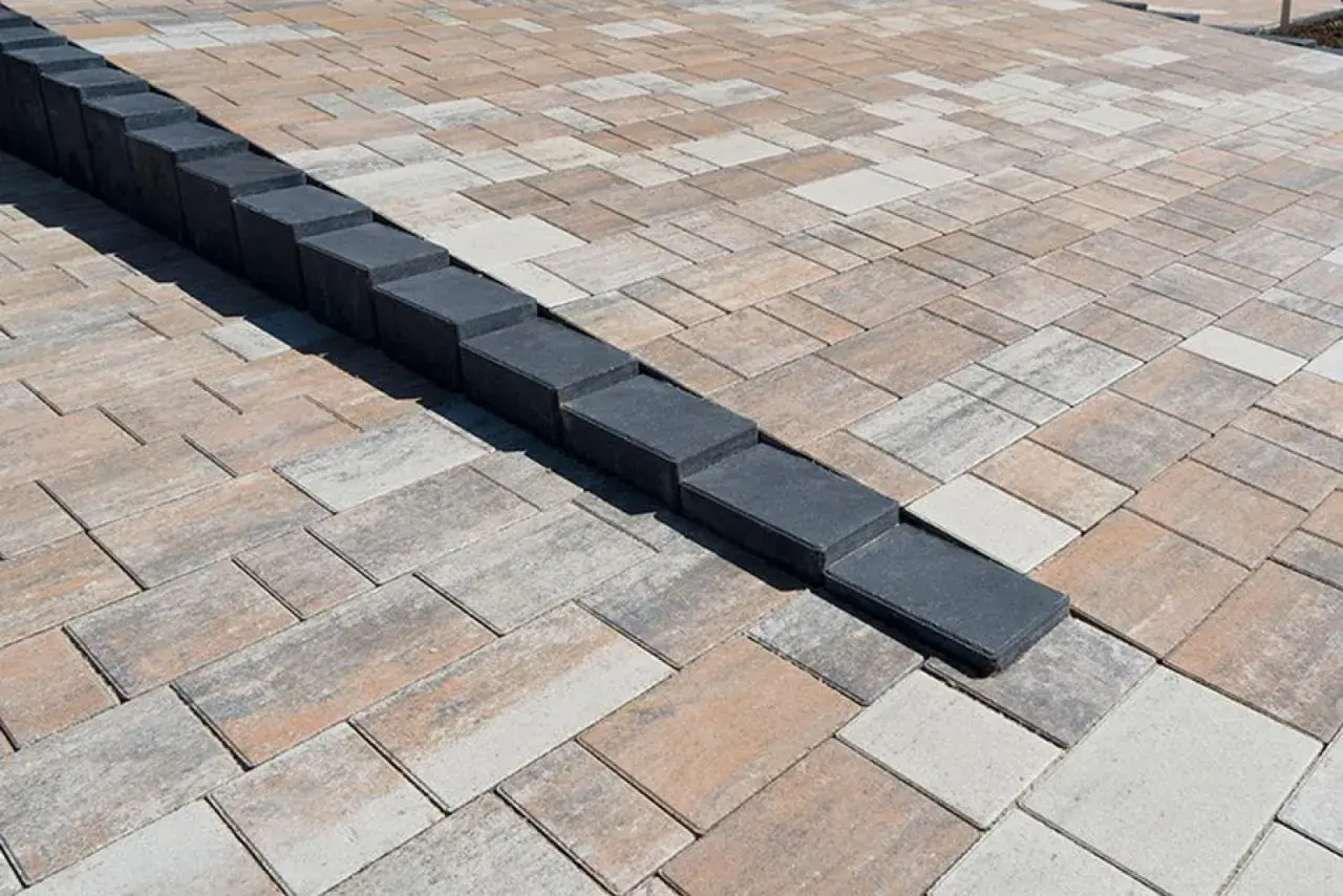 Nowa palisada z kostki brukowej tworzy elegancką linię na tarasie z kostki w odcieniach beżu i szarości.