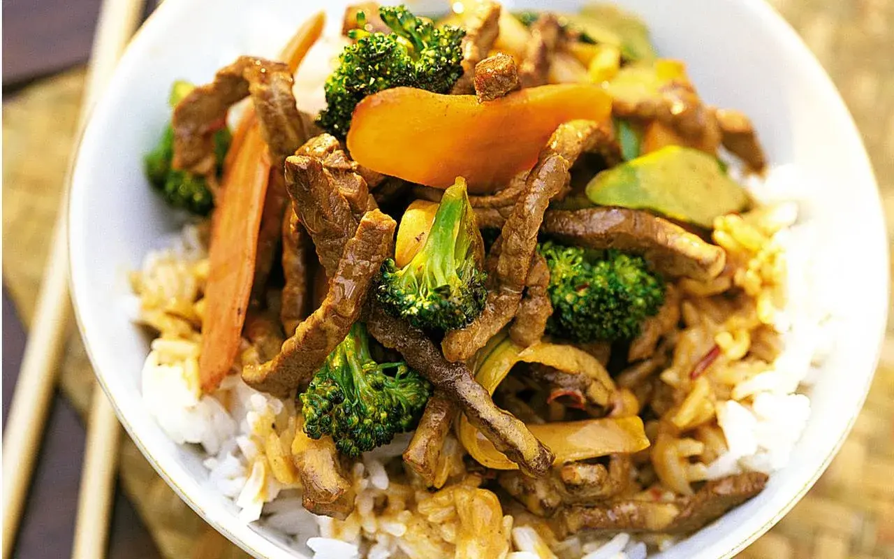 En skål med ris toppad med strimlad biff teriyaki, broccoli och morötter. En härlig asiatisk rätt.