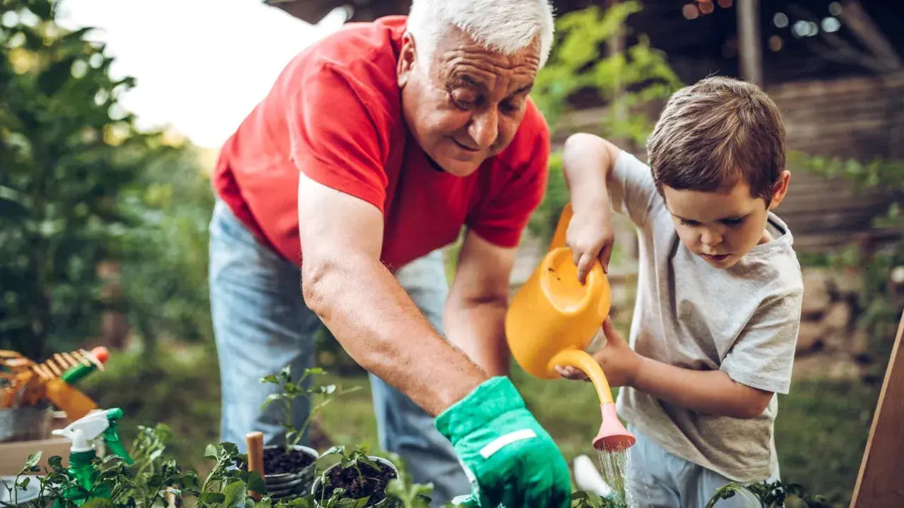 Nonni che vogliono stare soli con i nipoti, in giardino, insegnano a innaffiare le piantine.
