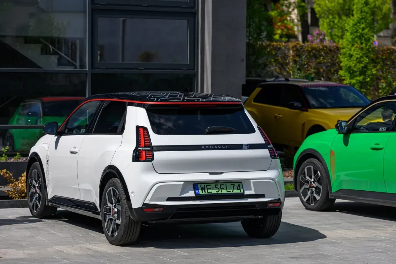 Biały Renault 5 E-Tech elektryczny z czarnym dachem i czerwonymi akcentami, obok zielonego i żółtego samochodu.