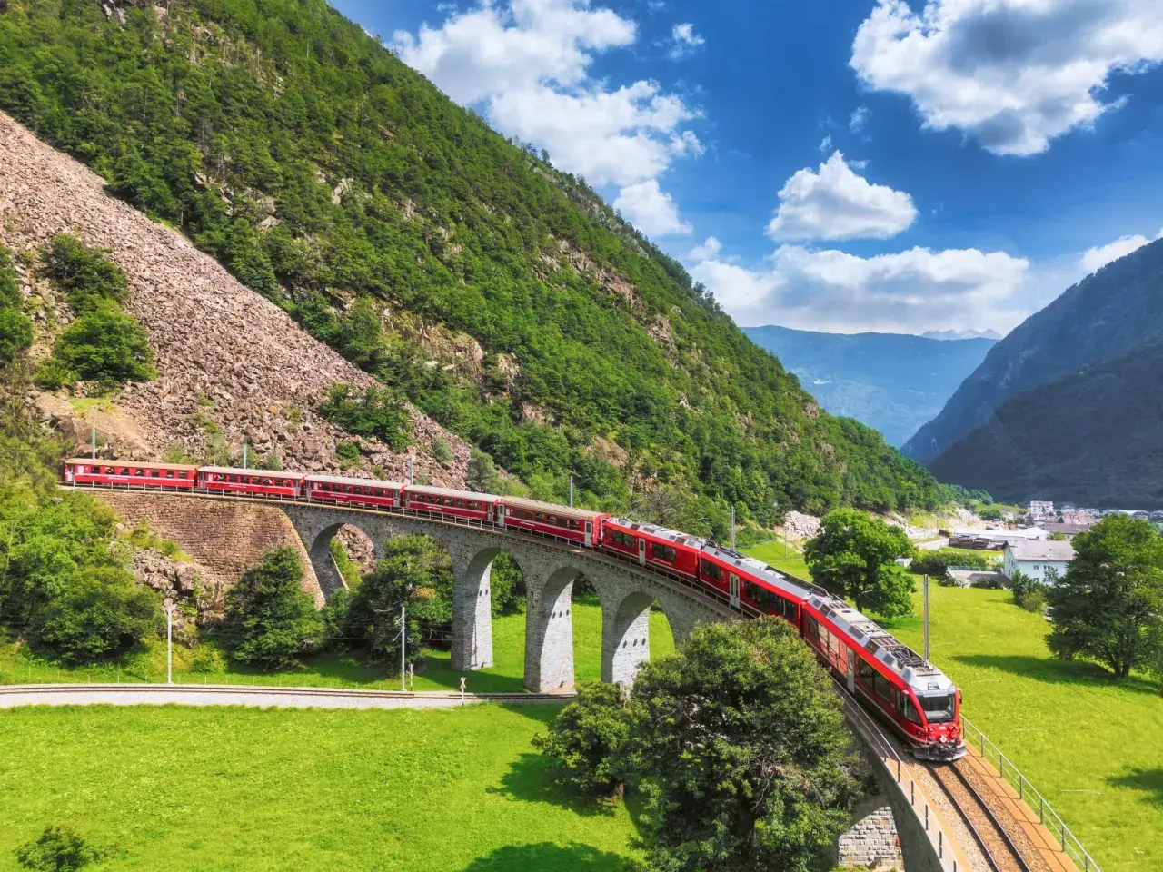 Czerwony pociąg Bernina Express na kamiennym wiadukcie, malownicza trasa i ceny podróży przez Alpy.