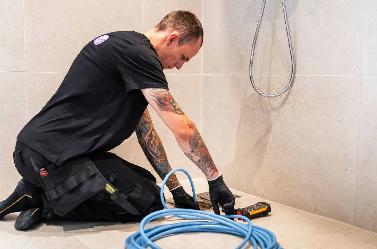 En rörmokare med tatueringar arbetar med en spolbil. Kostnad för spolbil kan variera beroende på problem.