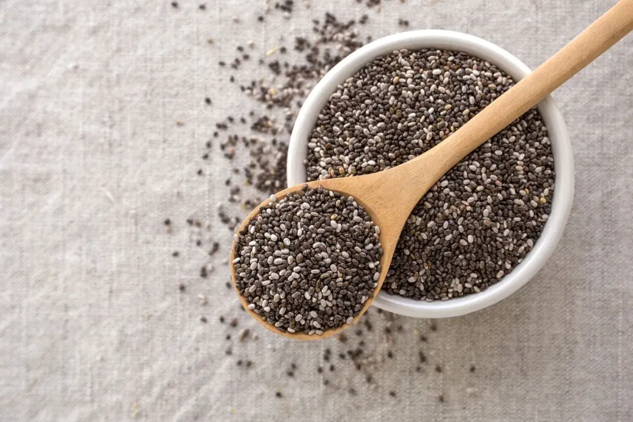 Semi di chia in una ciotola e cucchiaio di legno, un aiuto naturale per sgonfiare la pancia.