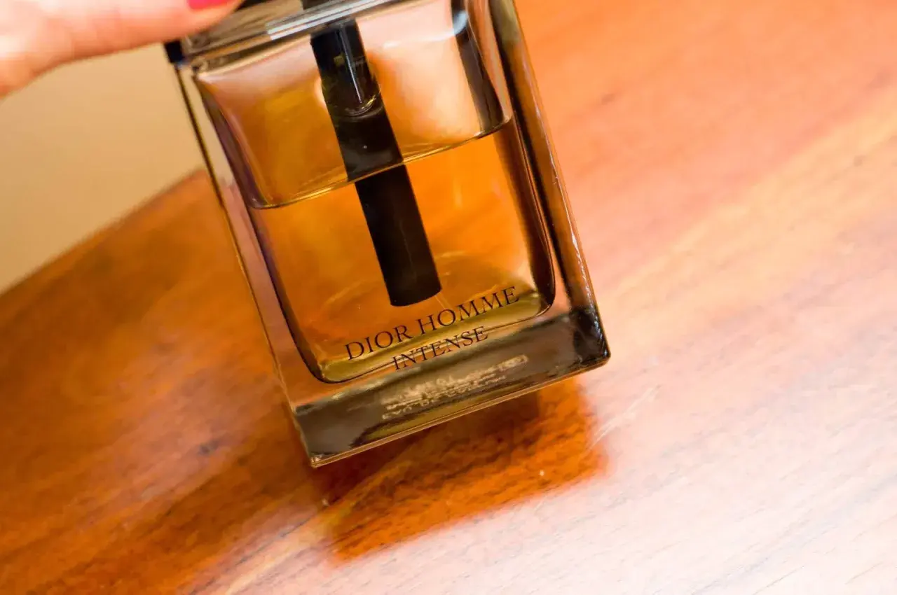 Elegancka butelka Dior Homme Intense z bursztynowym płynem na drewnianym blacie.