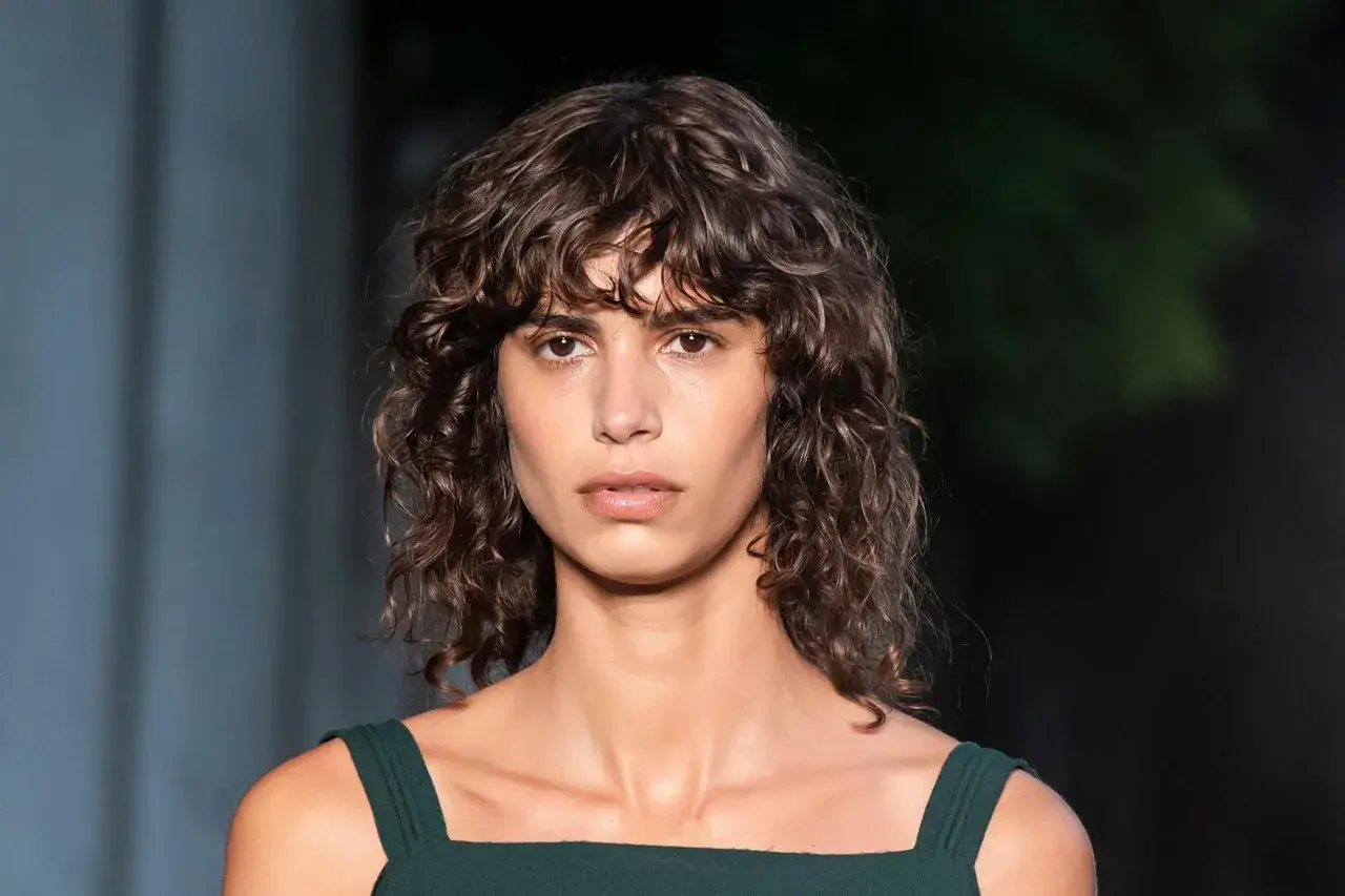 Modelo con cabello castaño ondulado y flequillo rizado, luciendo un vestido verde oscuro.