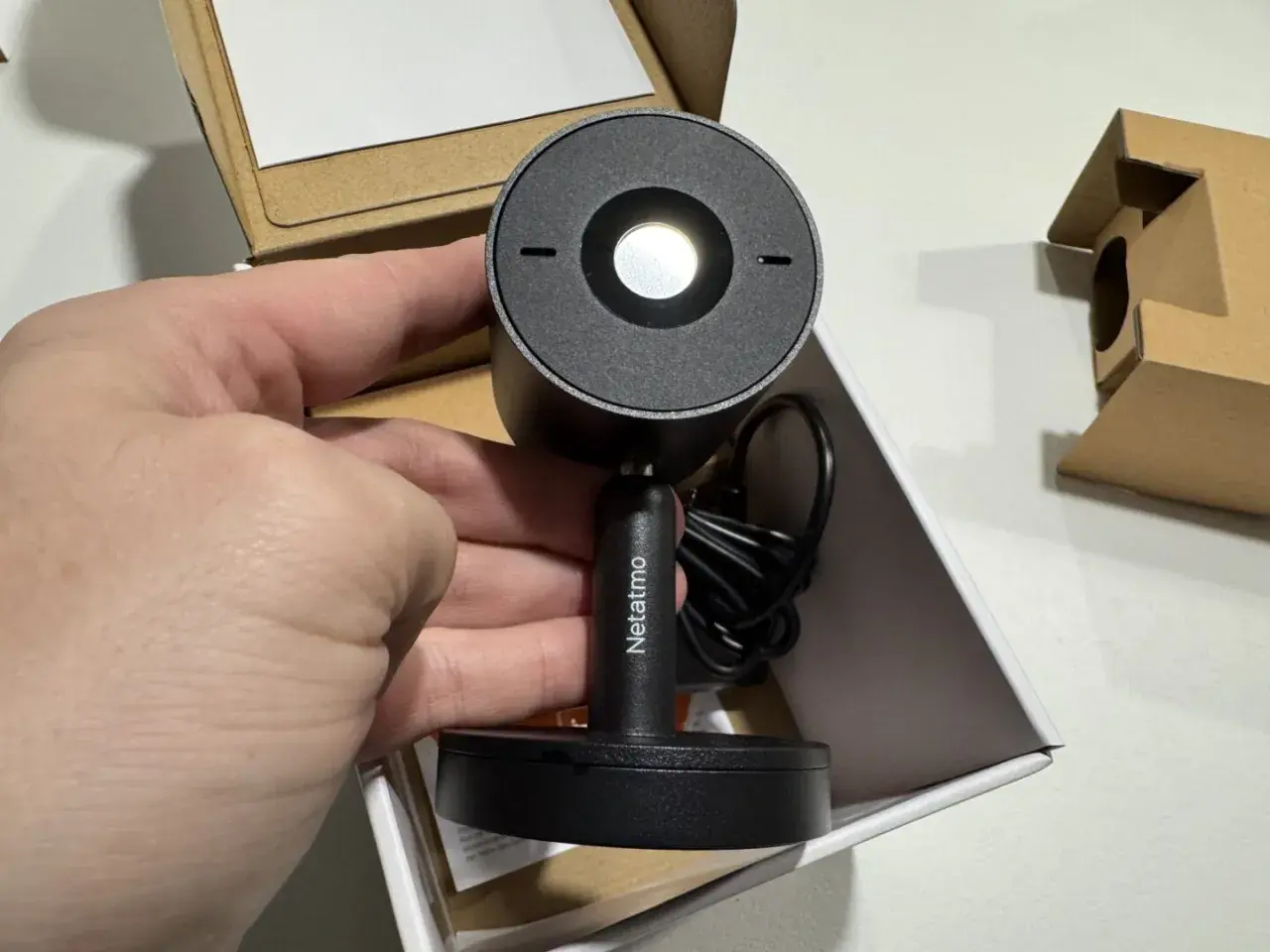 Main tenant de la nouvelle installation camera Netatmo. Le produit est dans sa boîte, prêt à être mis en place.