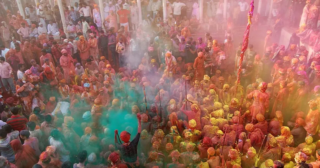 Tłum ludzi w kolorowych strojach, obsypany proszkami podczas święta Holi w Indiach.