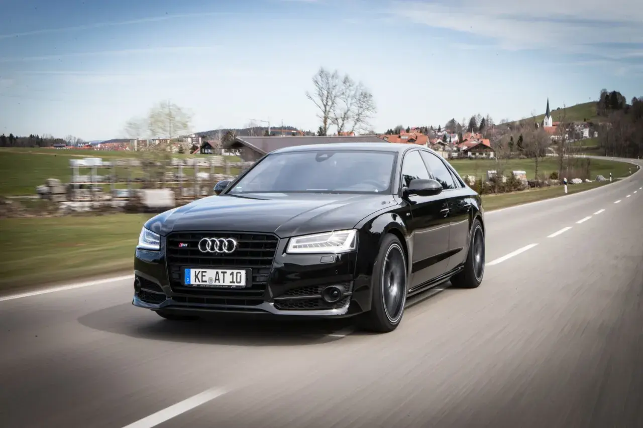 Czarny Audi RS8 pędzi po krętej drodze, mijając malowniczą wioskę.