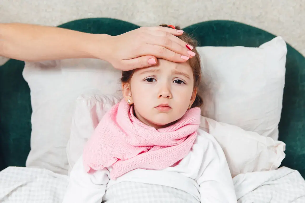 Bambina a letto con sciarpa rosa, mano sulla fronte per controllare la febbre, forse la quarta malattia.