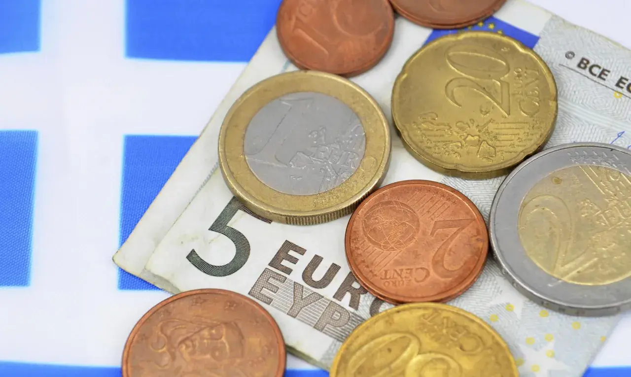 Euro to waluta w Grecji. Monety i banknot 5 euro na tle greckiej flagi.