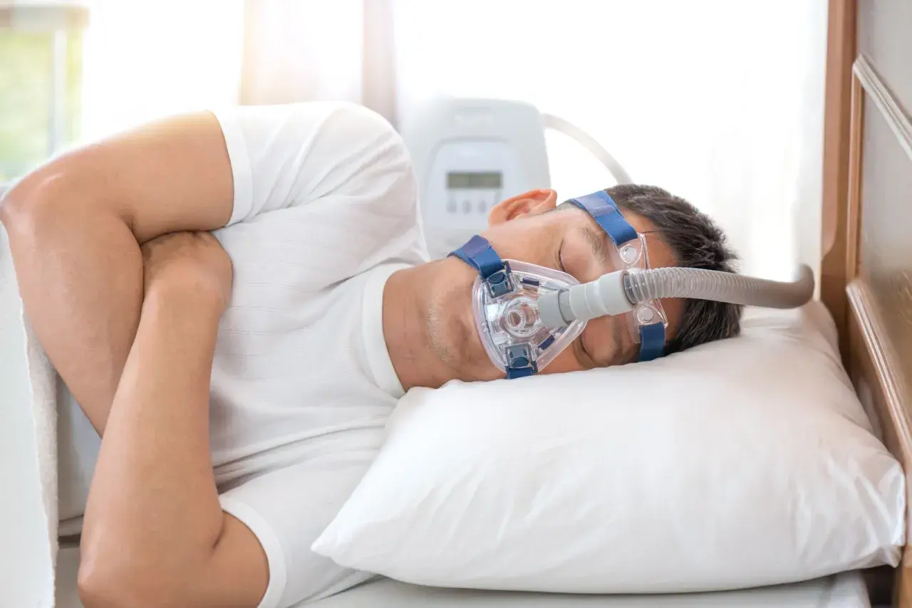 Mann mit Schlafmaske und CPAP-Gerät, ein Zeichen für die Behandlung von Schlafapnoe, wie von einem Schlafapnoe Arzt empfohlen.
