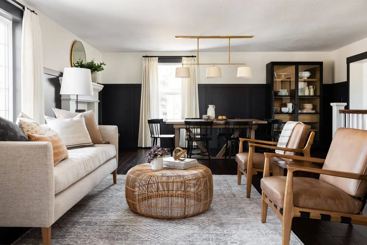 A living and dining space with a neutral palette and natural textures, embodying the mcgee and co style. A light-colored sofa, rattan coffee table, and leather armchairs create a cozy seating area.