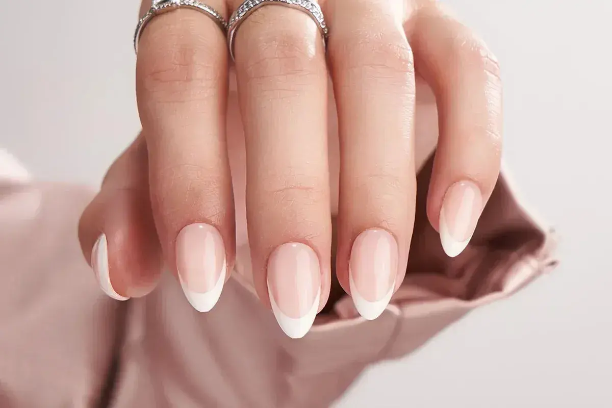 En hand med eleganta, korta french naglar och två glittrande ringar.