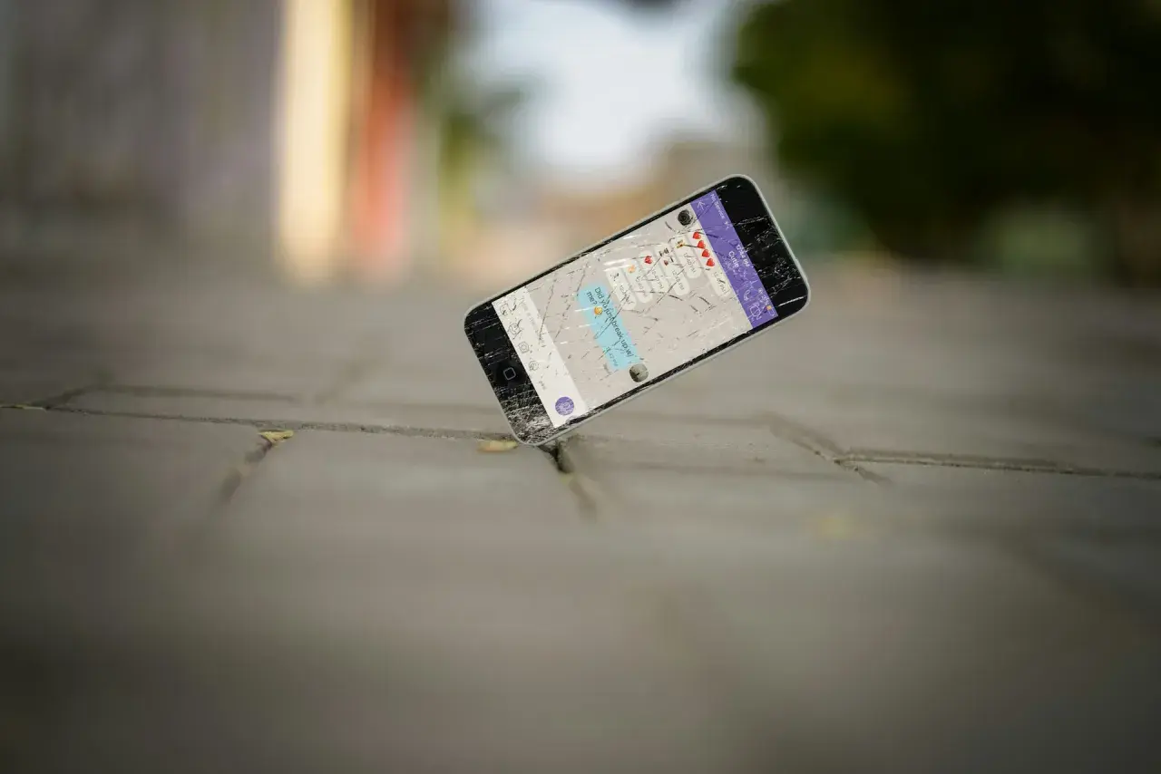 Zgubiony telefon z pękniętym ekranem leży na chodniku. Na wyświetlaczu widać wiadomość: "Did you just break up w/ me?".