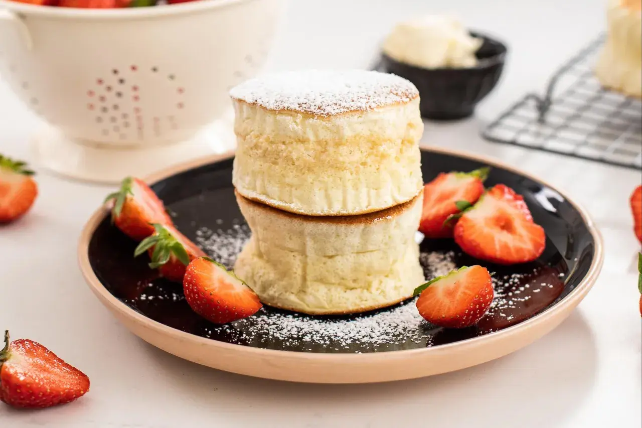Två fluffiga amerikanska pannkakor staplade på en tallrik med färska jordgubbar och pudersocker.