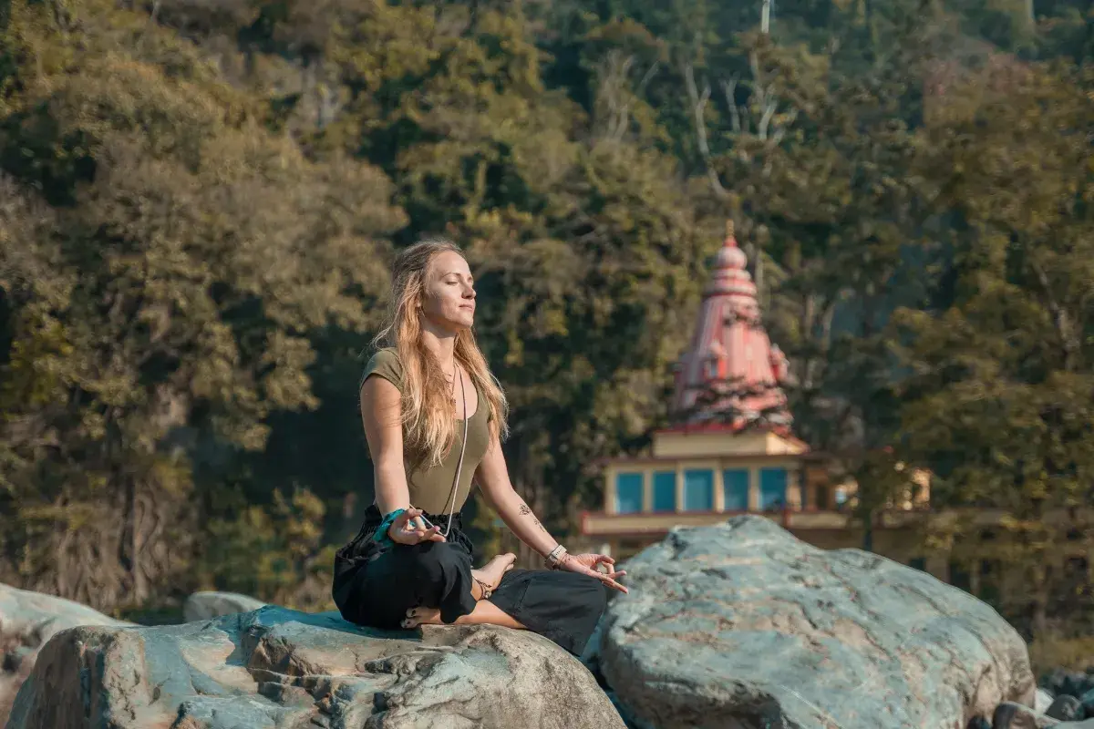 Mujer meditando en postura de loto sobre rocas, con un templo al fondo. Un momento de paz y el despertar de la conciencia.