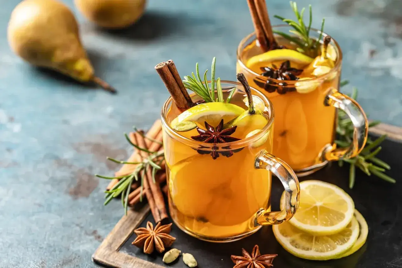 Zwei Gläser mit einem warmen Hot Toddy Rezept, garniert mit Zimt, Sternanis, Zitrone und Birne.