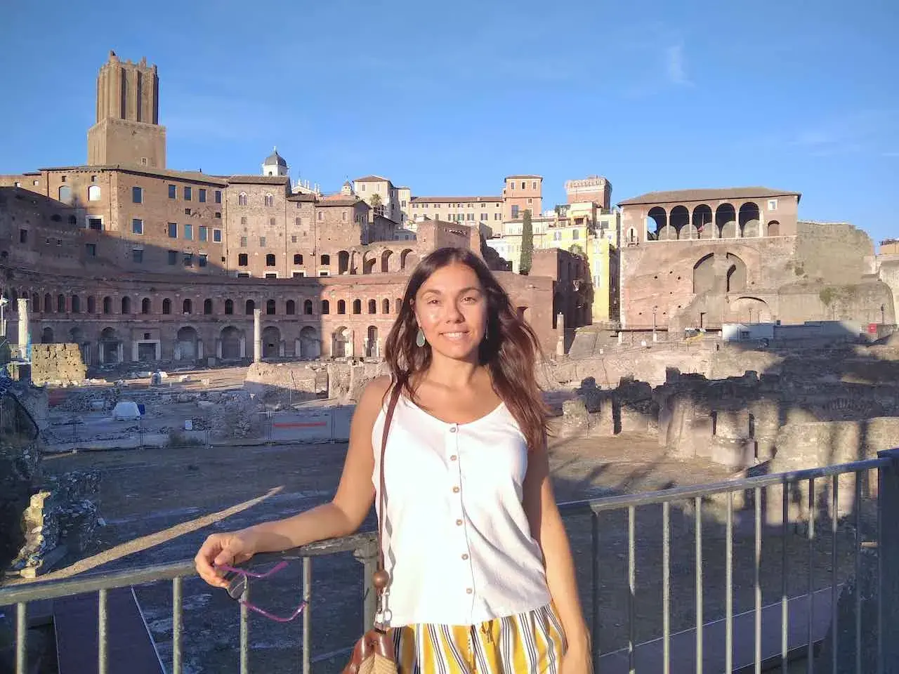A woman smiles in front of ancient Roman ruins, enjoying a sunny day. This scene suggests that Rome is safe and welcoming for tourists.