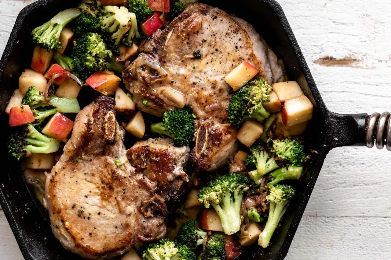 Juicy miso pork chops with roasted broccoli and apple chunks in a cast iron skillet.
