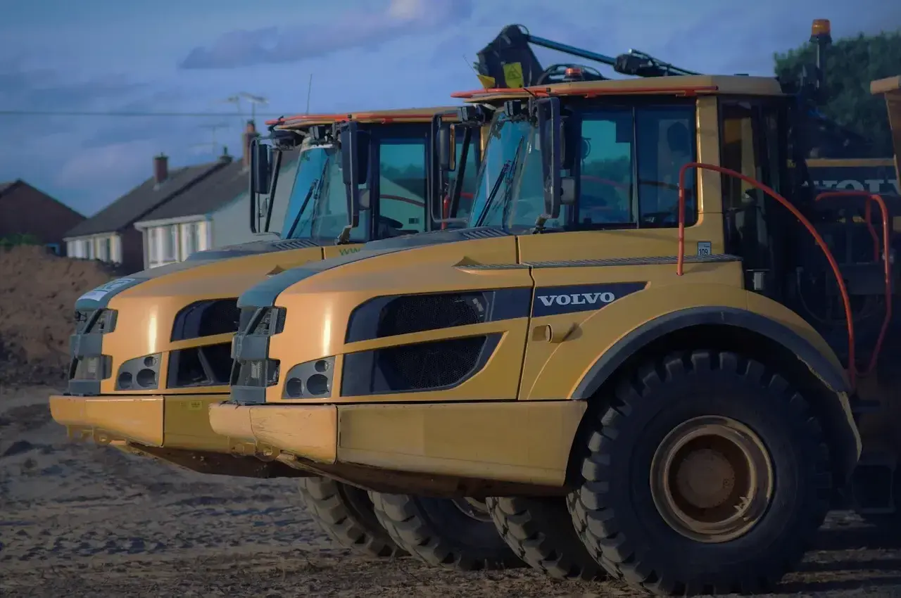 Dwa żółte wywrotki Volvo A30D stoją obok siebie. W tle domy i niebo.