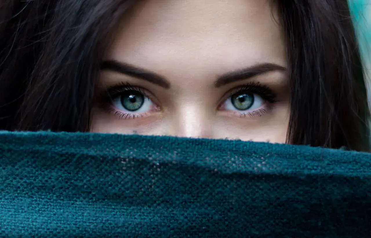 Ojos verdes penetrantes, enmarcados por cabello oscuro y un pañuelo. Un vistazo a la belleza que el microblading puede realzar.