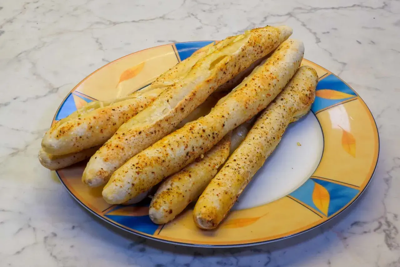 Leckere, knusprige brotstangen aus pizzateig, bestreut mit Gewürzen, liegen auf einem bunten Teller.