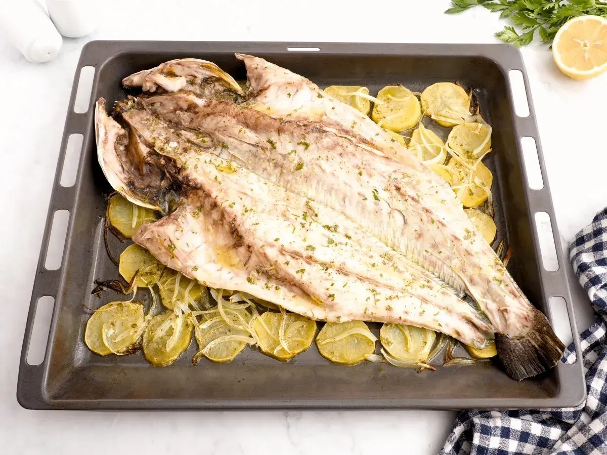 Corvina entera asada con patatas y limón en una bandeja. Una deliciosa opción para tus recetas de corvina.