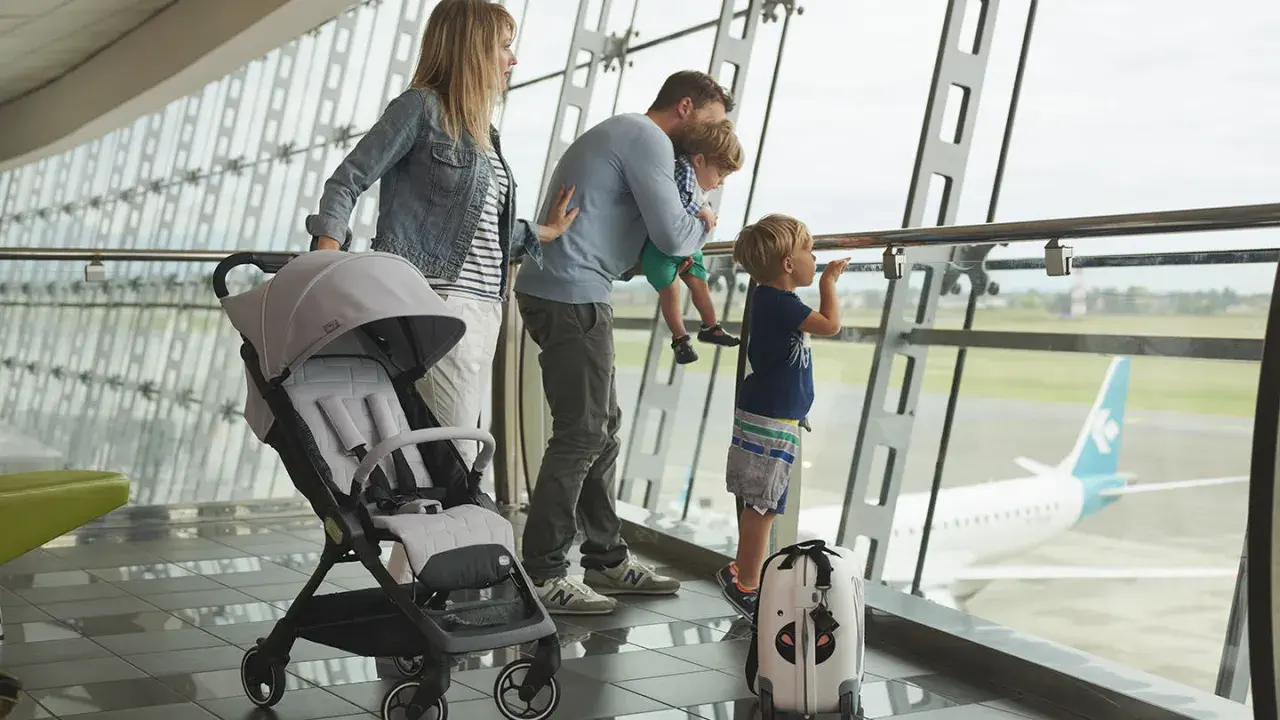 Famiglia in aeroporto, con passeggino e valigia, guarda un aereo. Speriamo che i bambini non soffrano di mal d'aereo!