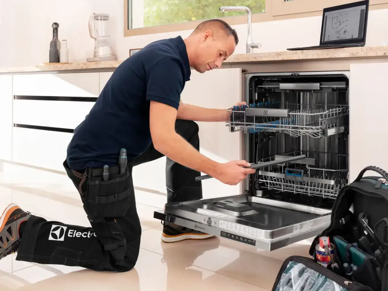 Serwisant w ubraniu z logo Electrolux naprawia zmywarkę. Electrolux to znana firma produkująca sprzęt AGD.