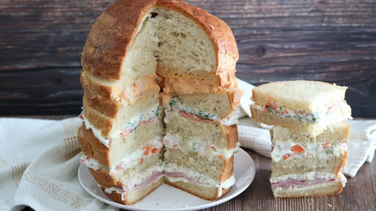 Un monumentale pane gastronomico a più strati, farcito con salmone, verdure e salse cremose, accanto a una versione più piccola.