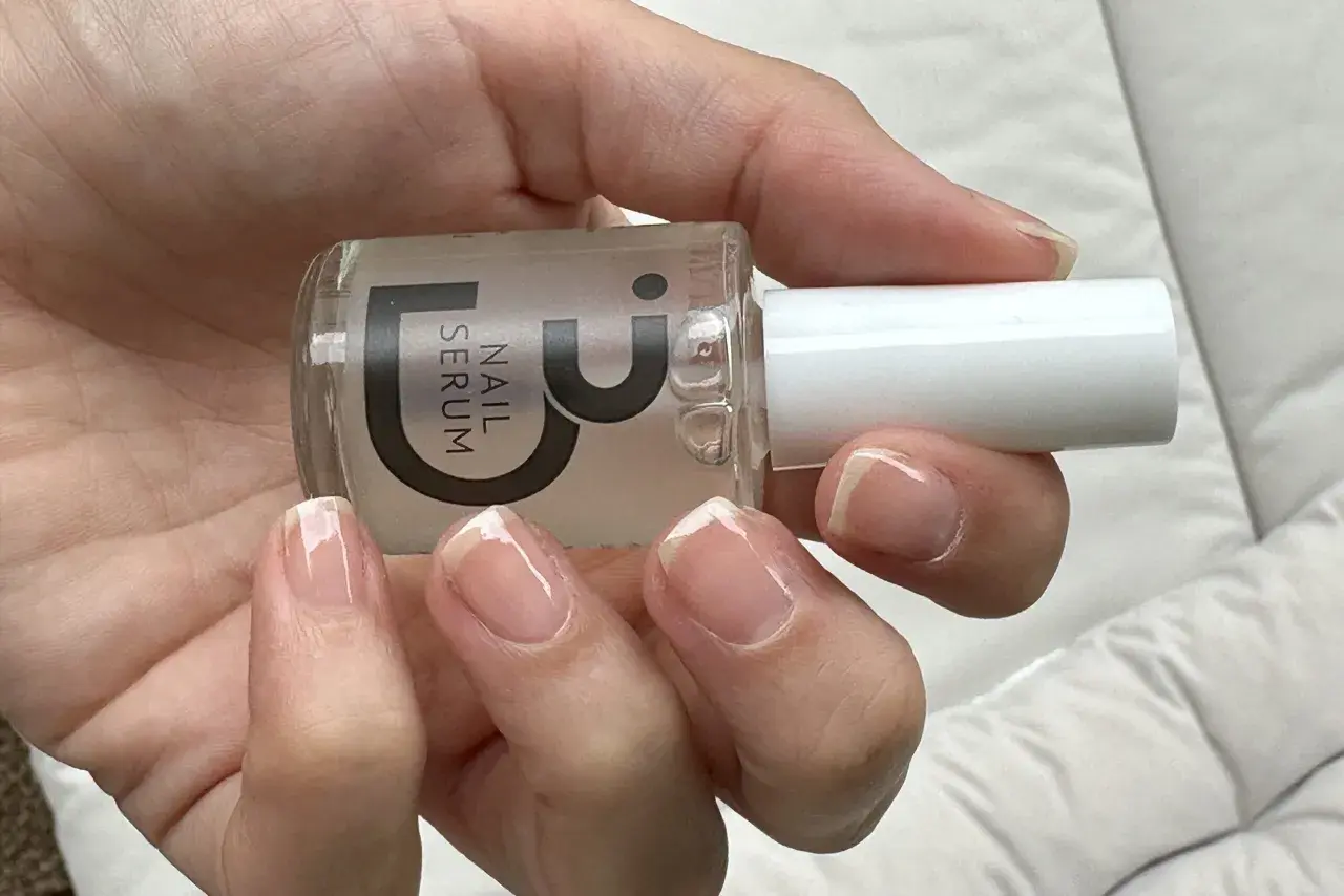 En hand håller en flaska nagelserum. Naglarna ser naturligt starkare och glansiga ut.