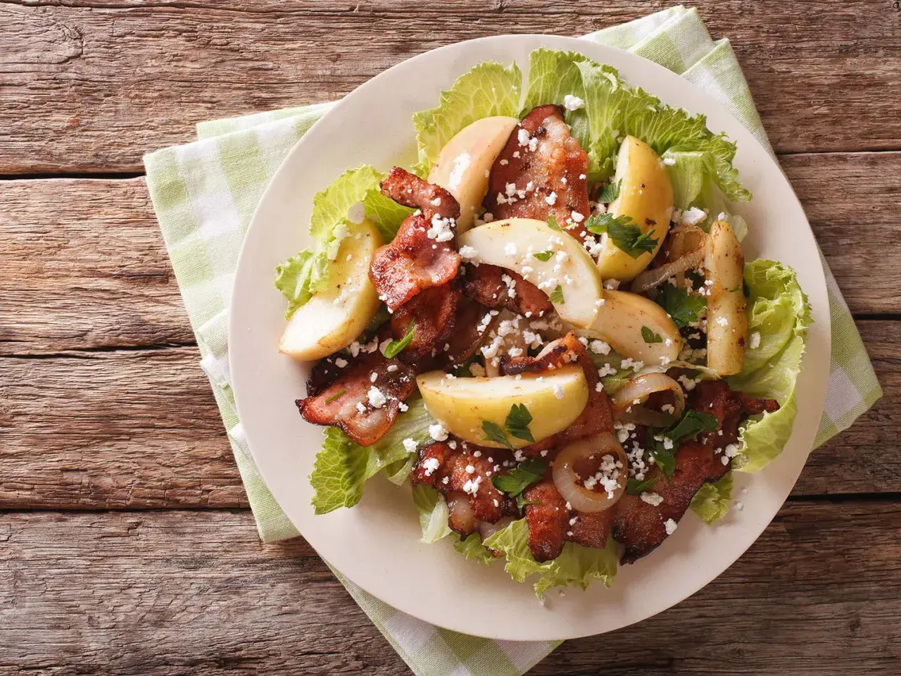 Une délicieuse idée de salade composée : lard croustillant, pommes de terre rôties, oignons caramélisés et fromage émietté sur un lit de laitue.