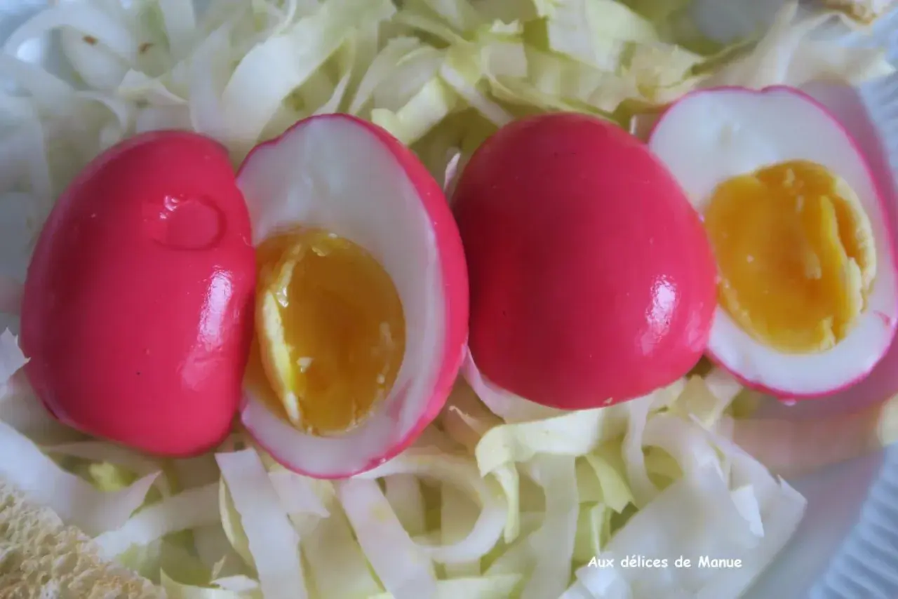 Trois œufs durs à la coquille rose vif, dont deux coupés révèlent un jaune d'œuf coulant, servis sur un lit de chou blanc émincé.