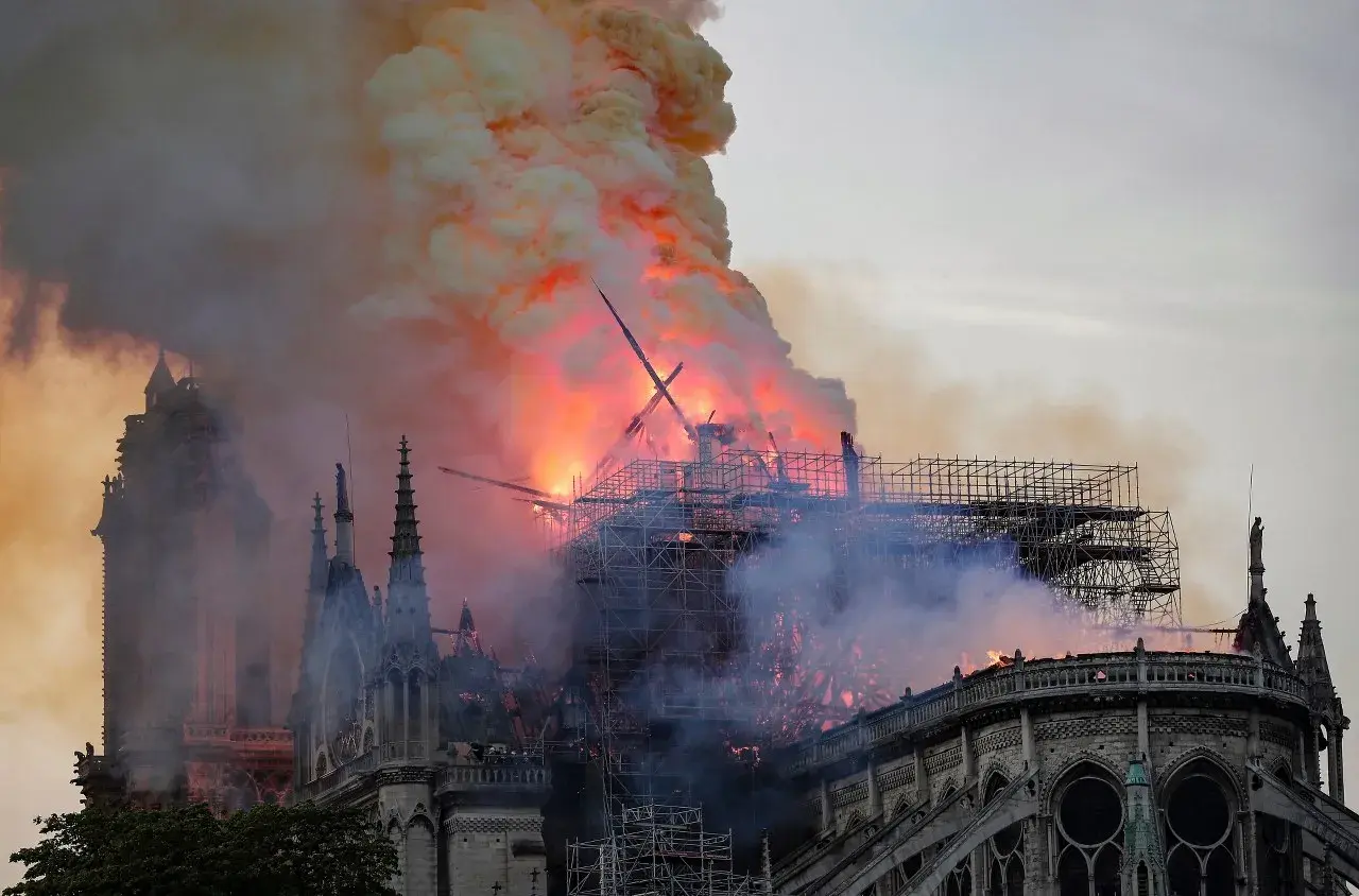Notre Dame pożar: płomienie trawią dach katedry, unoszą się kłęby dymu. Widoczne rusztowania i zniszczona konstrukcja.