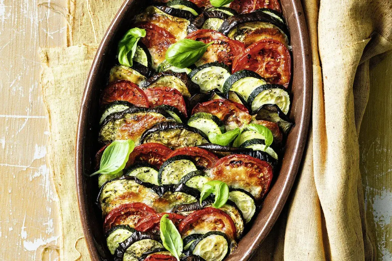 Gebackenes Gemüse aus Auberginen, Zucchini und Tomaten in einer Auflaufform, garniert mit Basilikum.
