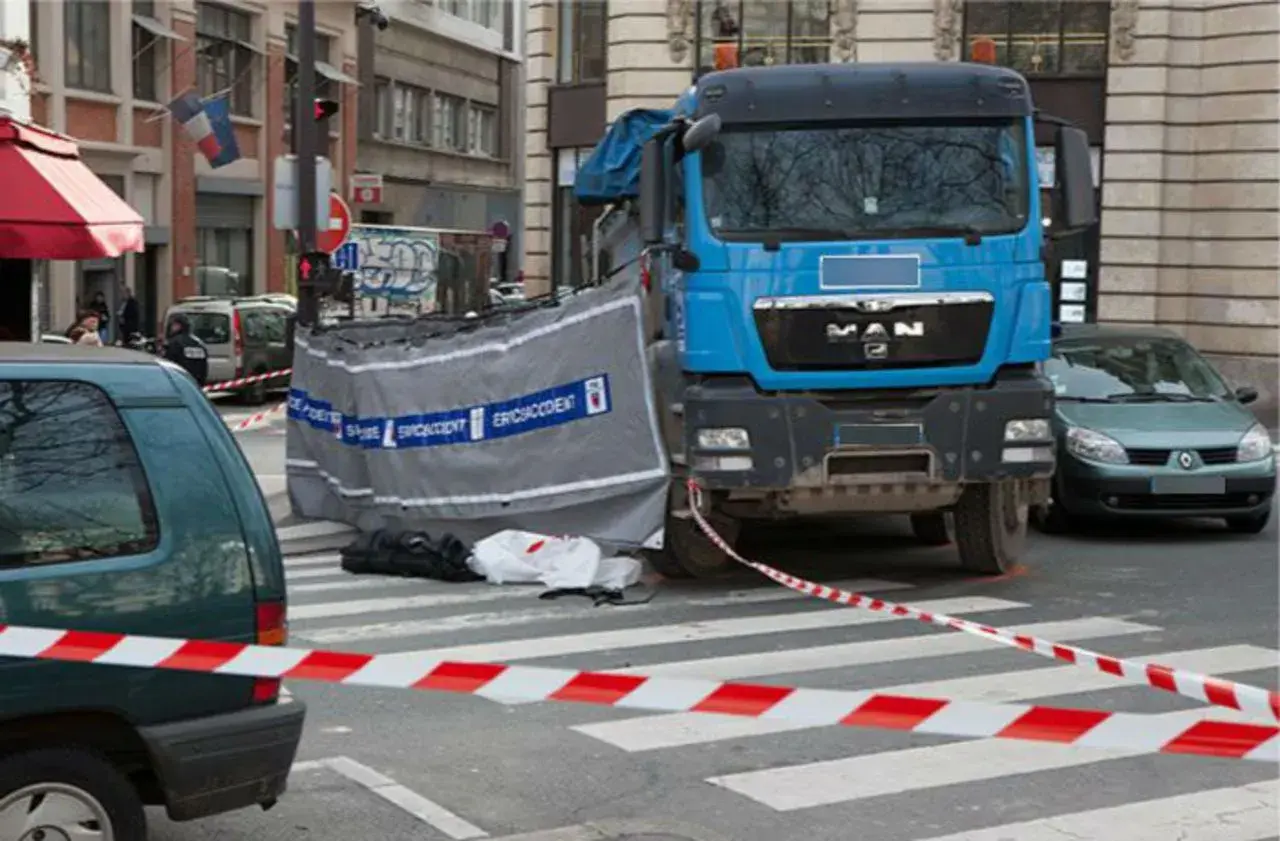 Scène d'accident avec camion bleu, voiture verte et ruban de sécurité. Un autocollant angle mort Europe est visible sur le camion.