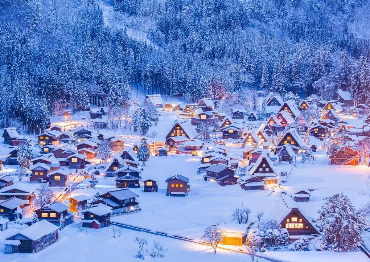 Ein verschneites Dorf in Japan im Winter. Traditionelle Häuser mit warmem Licht sind von schneebedeckten Bäumen umgeben.