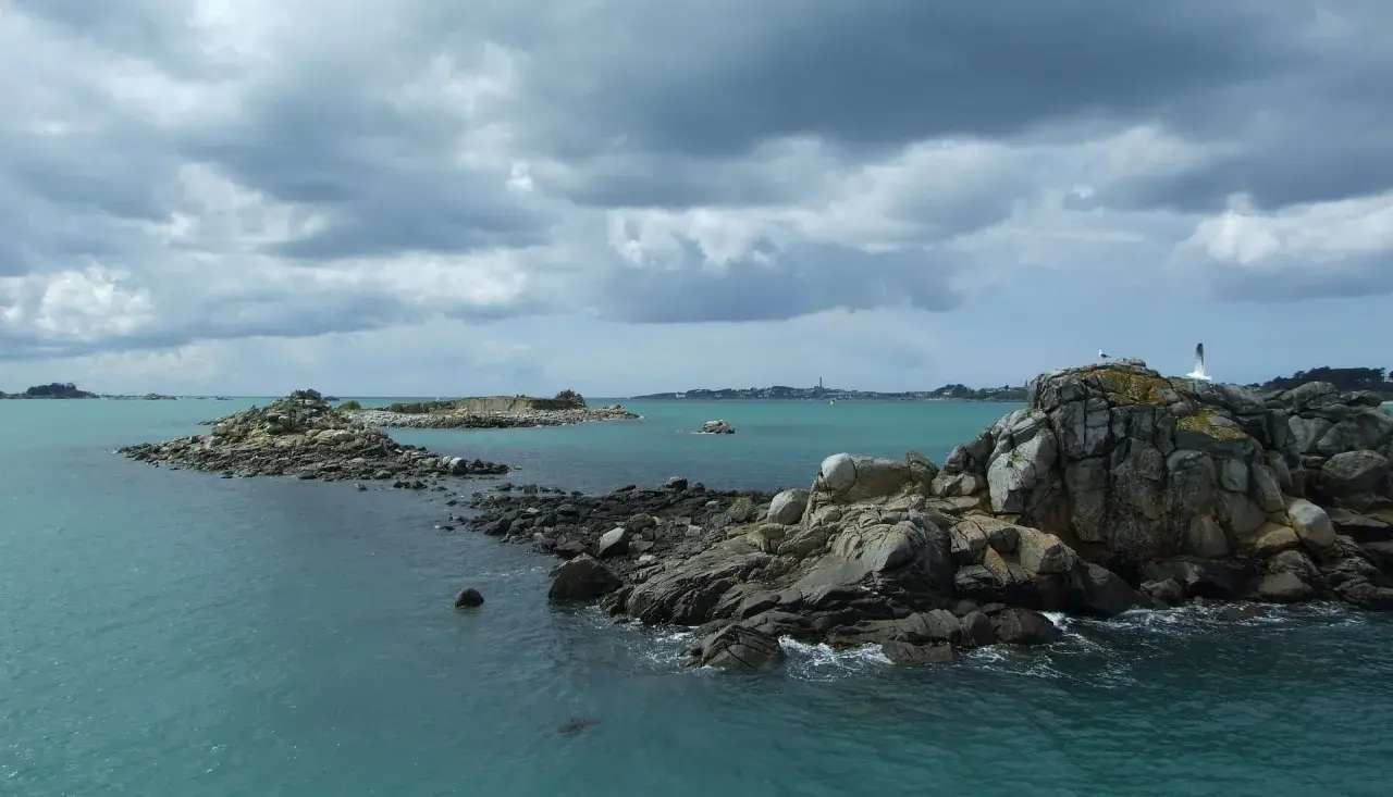 Îles rocheuses et mer turquoise près de Douarnenez, avec la Pointe du Raz en arrière-plan sous un ciel menaçant.