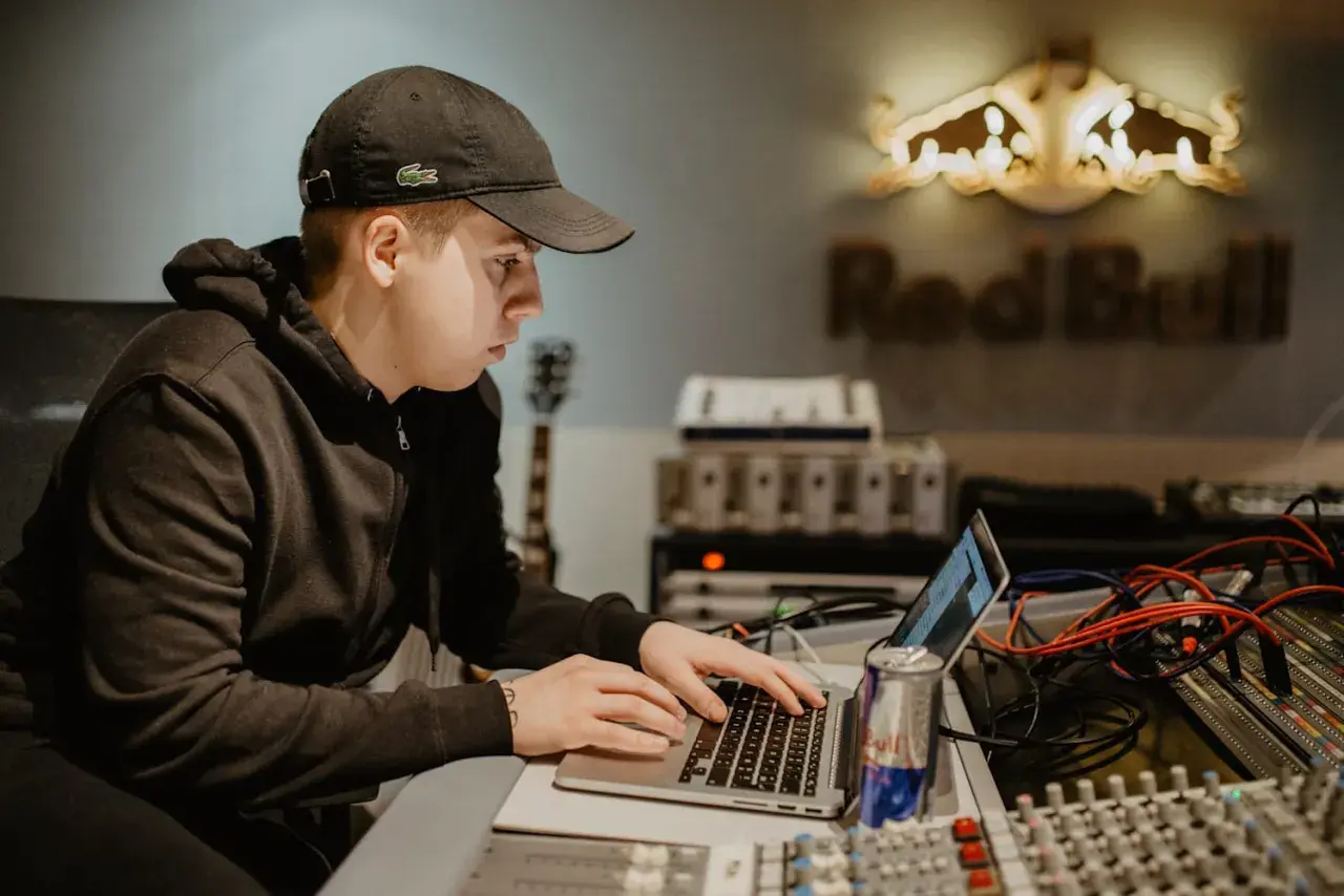 Un jeune beatmaker français concentré sur son ordinateur portable dans un studio d'enregistrement, une canette Red Bull à portée de main.
