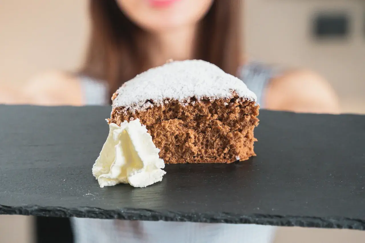 Una fetta di pan di spagna al cacao, soffice e spolverata di zucchero a velo, servita con panna montata su una lavagna scura.