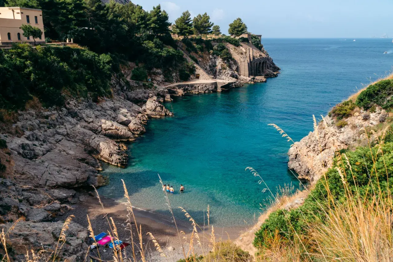 Una piccola spiaggia a Sorrento, con acque cristalline e rocce scoscese. Alcune persone si rinfrescano in mare.