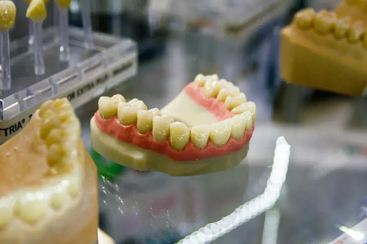 Modello di dentiera mobile con denti bianchi e gengive rosa su un piano di vetro.