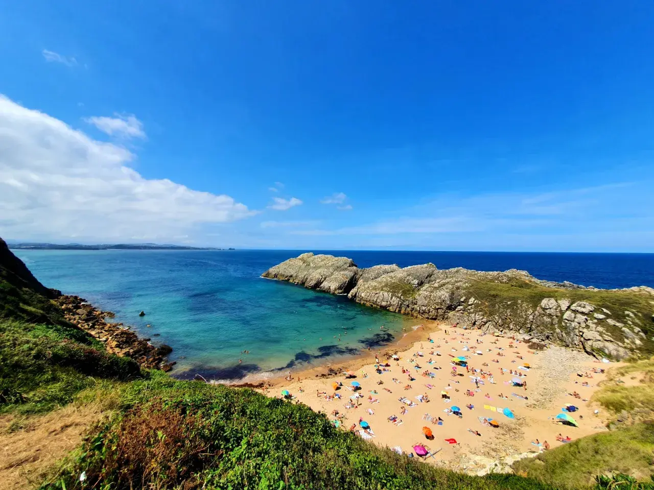 Vista aérea de la playa de Somo, con gente disfrutando del sol y el mar. Las reseñas de la playa de Somocuevas la describen como un paraíso.