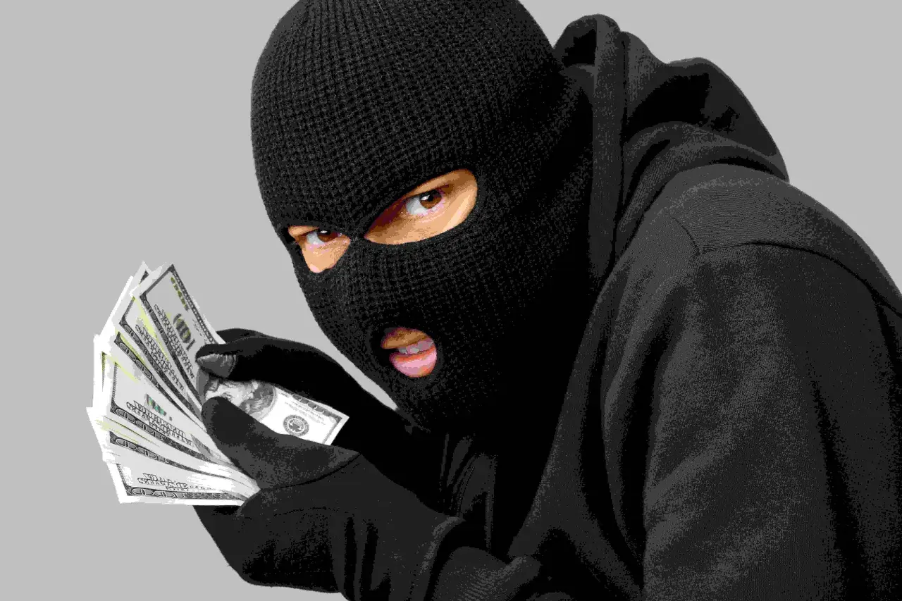 Un individu masqué, vêtu d'un sweat à capuche, compte des liasses de billets. Le vol a visiblement bien réussi.