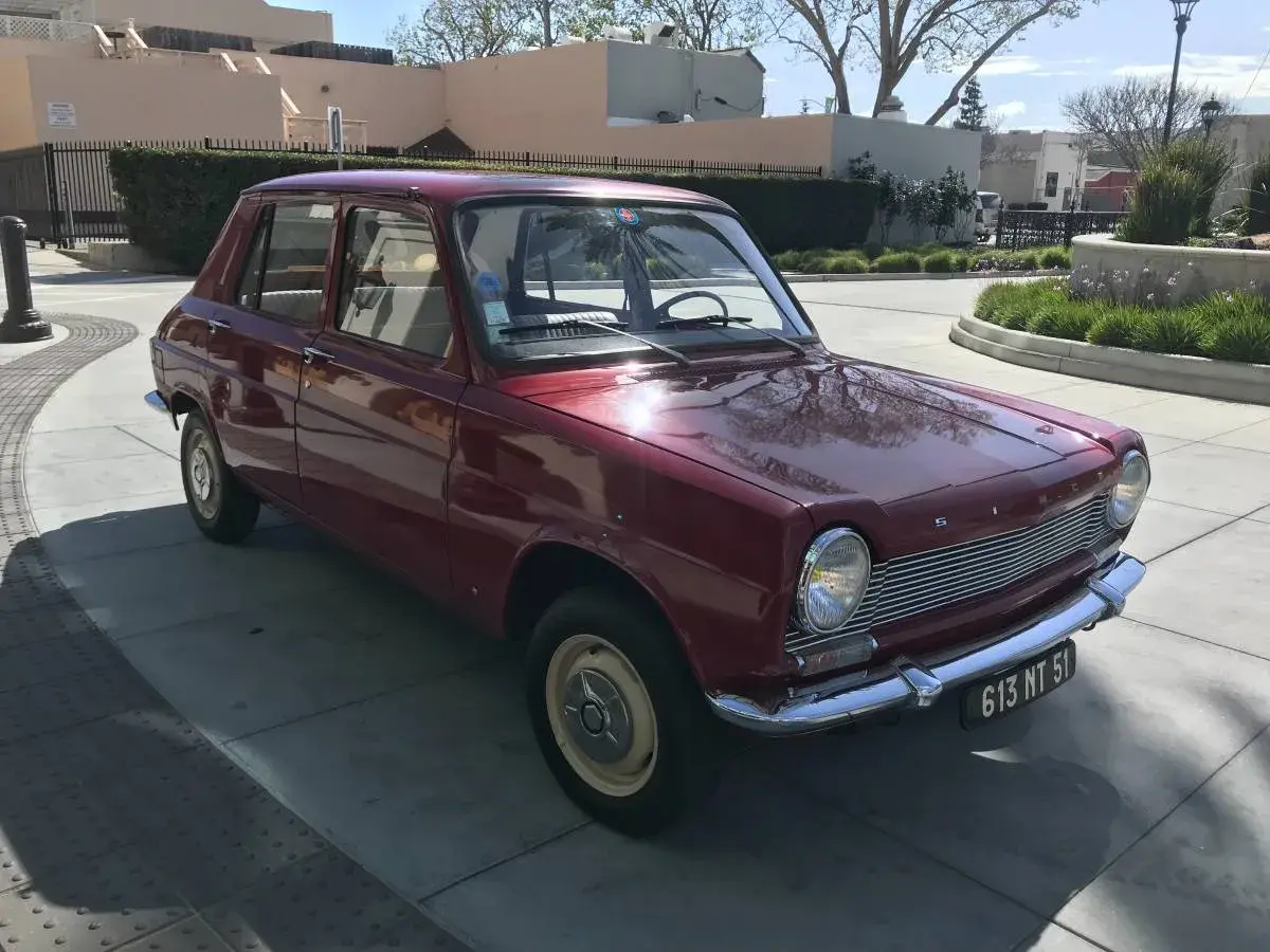 En röd Simca 1100 står parkerad på en solig uppfart.