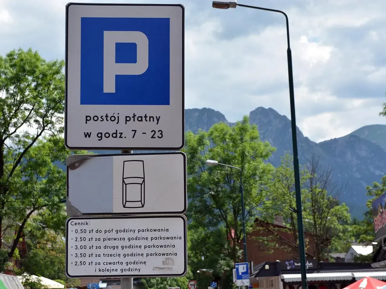 Znaki parkingowe w Zakopanem, informujące o płatnym postoju i cenniku. W tle góry i drzewa, idealne na trasę do skoczni.