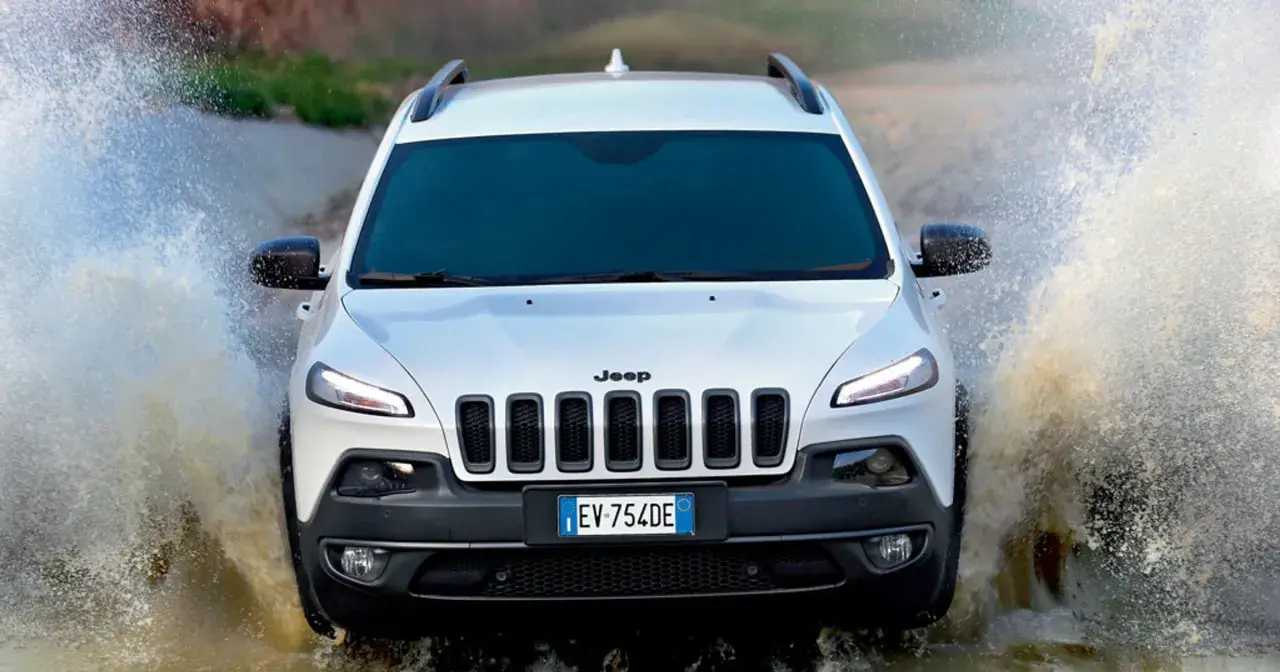 Biały Jeep Cherokee Trailhawk z impetem wjeżdża w wodę, tworząc efektowne rozbryzgi.